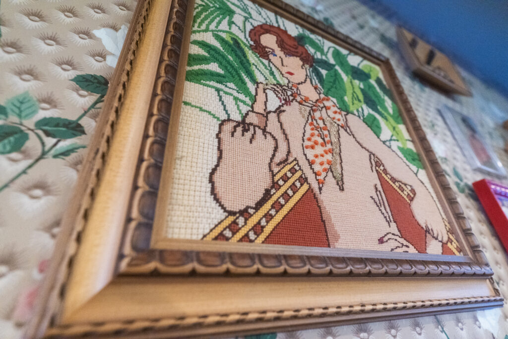 photo of framed cross stitch art of a woman in front of plants displayed in restaurant