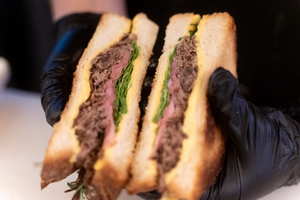 toasted sandwich with greens, pickled onion and roast beef held by chef hands