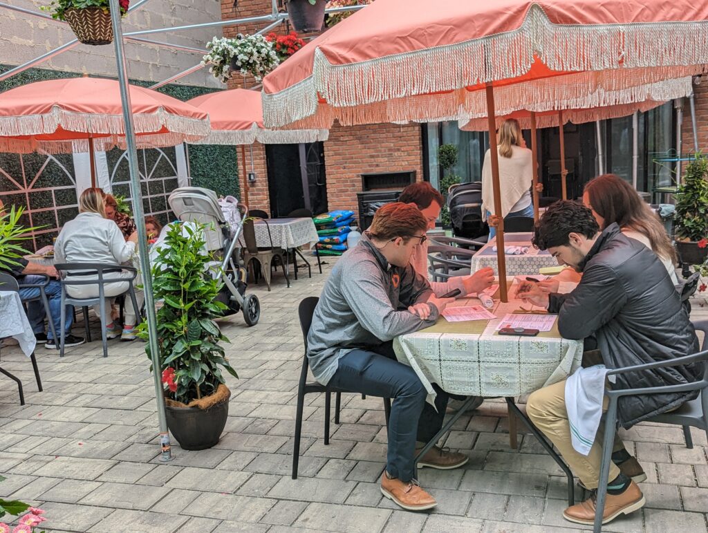 customers sitting outside and looking at menus at tables with red umbrellas.